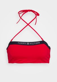 Top de bikini vermelho com uma faixa preta, apresenta alças cruzadas ajustáveis e o logótipo "TOMMY HILFIGER" na parte da frente. Textura de tecido suave.