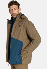 Veste imperméable avec un design coloré en blocs de marron et bleu, une capuche, des poches zippées et des accents turquoise contrastants.