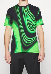 Camiseta de manga corta en negro y verde vibrante con un patrón ondulado. Confeccionada en tela suave, presenta un escote redondo y un corte relajado.