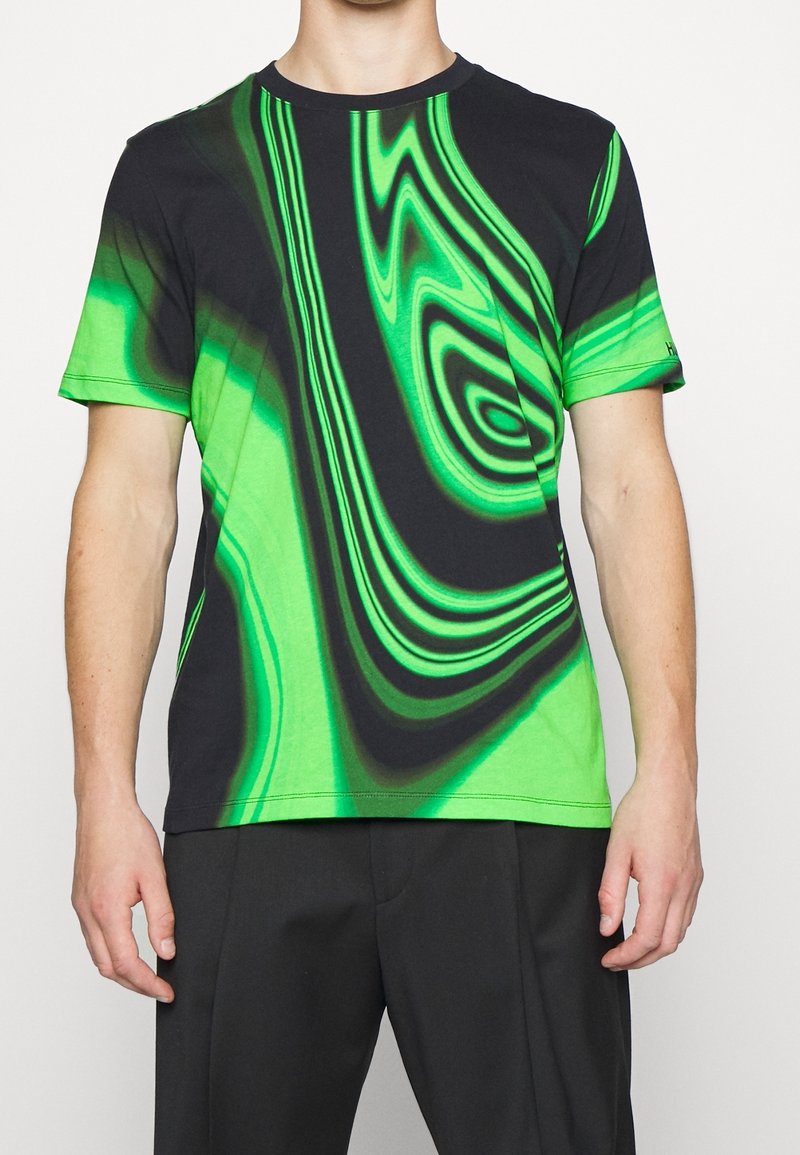 Camiseta de manga corta en negro y verde vibrante con un patrón ondulado. Confeccionada en tela suave, presenta un escote redondo y un corte relajado.