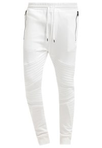 Bílé zúžené tepláky s žebrovanými bočními panely, elastickým páskem a zipovými kapsami. Vyrobené z hladkého, elastického materiálu.