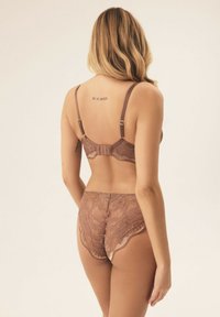 Lace bra and panty set in soft taupe, featuring adjustable straps, floral patterns, and a hook-and-eye closure at the back.