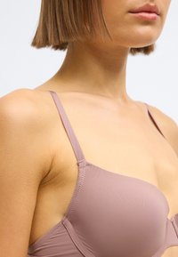 Svetlofialová podprsenka s hladkou látkou, tenkými nastaviteľnými ramienkami a bezšvovým dizajnom. Vyznačuje sa jemným prešívaním pozdĺž okrajov.