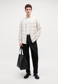 Bardžo ir baltos spalvos languota marškinėlių camisa, balta T-marškiniai, juodos džinsinės kelnės, juoda odinė rankinė ir juodi kulkšninių batai.