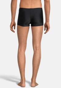 Schwarze Badeshorts aus glattem Material, mit niedrigem Bund und enger Passform, schlicht im Design ohne sichtbare Details.