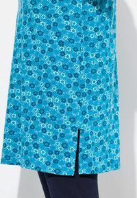Tunic turchese con motivo floreale in tonalità di blu e bianco, con uno spacchetto laterale all'orlo e una texture morbida.