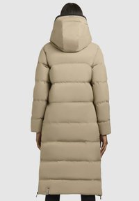 Giacca puffer beige con cappuccio, caratterizzata da un design trapuntato e maniche lunghe. L'orlo è leggermente curvato, con zip visibili nella parte inferiore.