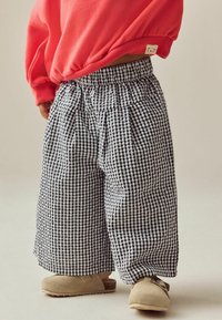 Pantaloni a gamba larga in gingham bianco e nero con vita elastica, abbinati a zoccoli in suede beige e un felpa corallo brillante.
