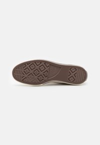 Semelle de sneaker en caoutchouc brun avec des motifs de crans en diamant et hexagonaux, présentant une bande latérale blanche et un bord texturé.