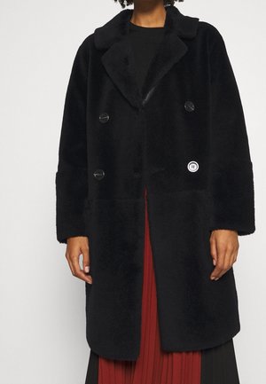 Cappotto nero doppiopetto realizzato in materiale plush, con colletto, grandi bottoni e una patch con logo sul davanti, caratterizzato da maniche ampie.