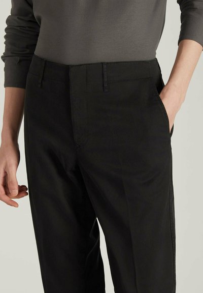 Pantaloni neri con una finitura liscia e opaca, caratterizzati da un design slim fit e tasche laterali. La vita ha una chiusura semplice, senza hardware visibile.