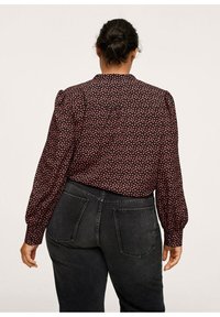 Blouse à manches longues avec un fond sombre, ornée de petits motifs floraux roses. Tissu doux, dos boutonné et manches légèrement bouffantes.