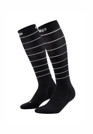 Zwarte kniekousen met grijze horizontale strepen, gemaakt van rekbaar materiaal voor comfort en ondersteuning. Logo zichtbaar nabij de bovenkant.