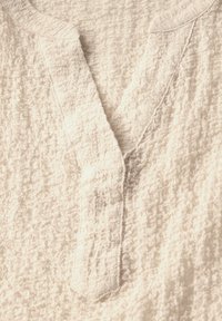 Crème textiel top met een v-halslijn en gestikte details langs de randen, met een zachte, gekreukte oppervlakte.