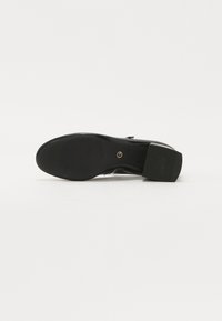 Semelle de chaussure en cuir noir avec talon et orteil texturés, petit logo circulaire près de la voûte plantaire, isolée sur fond blanc.
