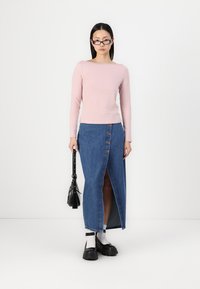 Lyserød langærmet top med firkantet udskæring, parret med en denimnederdel med høj slids og knapper. Kraftige sorte sko og en lille sort taske.
