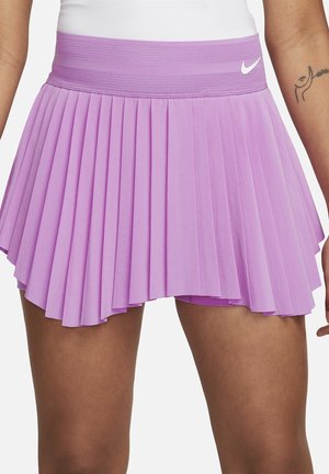 Vrouw draagt een paarse geplooide sportrok met een brede tailleband en wit Nike-logo aan de rechterkant.