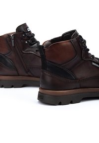Brown leather ankle boots with a textured finish, featuring a side zip, lace-up front, and rubber sole. Accented with dark panels.