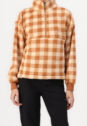 Person wearing a tan and cream checkered fleece pullover with a half-zip front and ribbed cuffs, paired with black pants.