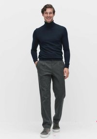 Marineblauwe coltrui, grijze broek en grijze sneakers. Strakke pasvorm, zachte textuur, met een neutraal palet en minimale details.