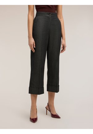 Donna che indossa pantaloni corti a vita alta grigio scuro con ampi risvolti e scarpe slingback con tacco alto color bordeaux, in piedi immobile.