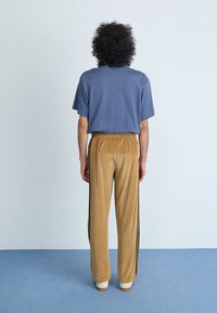 T-shirt azul de algodão com mangas curtas, combinada com calças de veludo leve castanho com riscas laterais pretas e cintura elástica.