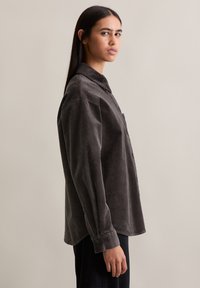 Szara koszula ze sztruksu z zapięciem na guziki, kołnierzem typu rozłożystego i długimi rękawami. Subtelna faktura, luźny krój, w zestawieniu z ciemnymi spodniami.