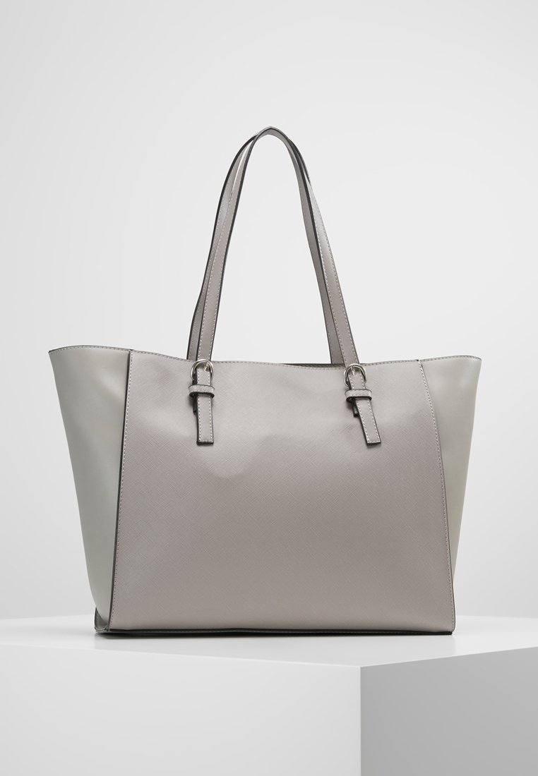 Sac cabas en cuir gris clair avec deux longues anses et des détails de boucles argentées, présenté sur une surface blanche sur un fond uni.