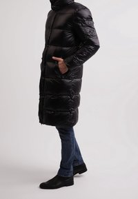 Černá péřová bunda s vysokým límcem, zipovými kapsami a prošívanou strukturou. Nositelná s modrými džíny a černými koženými botami.