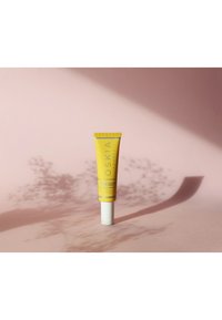 Gul kosmetiktub med ett vitt lock, märkt "OSKIA" och "Super 20 Vitamin Facial Cream", mot en mjuk rosa bakgrund med skuggor.