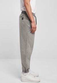 Šedé teplákové kalhoty s elastickým pasem a šňůrkou, s bočními kapsami a logem, doplněné bílými teniskami.