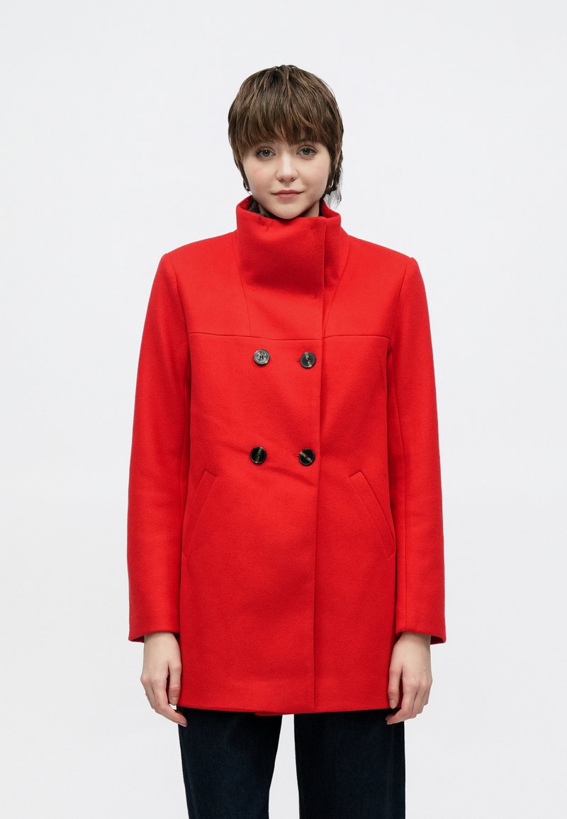 Red double-breasted coat with a high collar, made of wool fabric, featuring black buttons and side pockets, styled with minimal detailing.