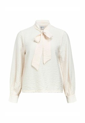 Blusa de manga larga en beige claro con una superficie texturizada, que presenta un lazo en el cuello y puños ajustados. Dobladillo redondeado.