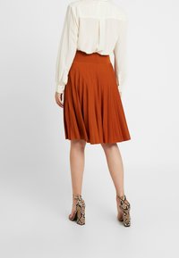 Sukně v rezavě červené barvě s plisováním a vysokým pasem, zkombinovaná s lehkou blůzkou a vysokými podpatky se vzorem hadí kůže.