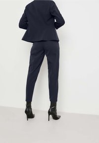 Granatowa marynarka o dopasowanym kroju z rozkloszowanym dołem noszona na dopasowanych spodniach w tym samym kolorze, w połączeniu z czarnymi botkami na obcasie, prezentująca elegancki, profesjonalny wygląd.