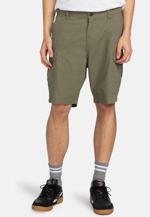 Khaki Cargo-Shorts mit mehreren Taschen, geradem Schnitt und Knopfverschluss. Kombiniert mit schwarzen Sneakern und grauen gestreiften Socken.
