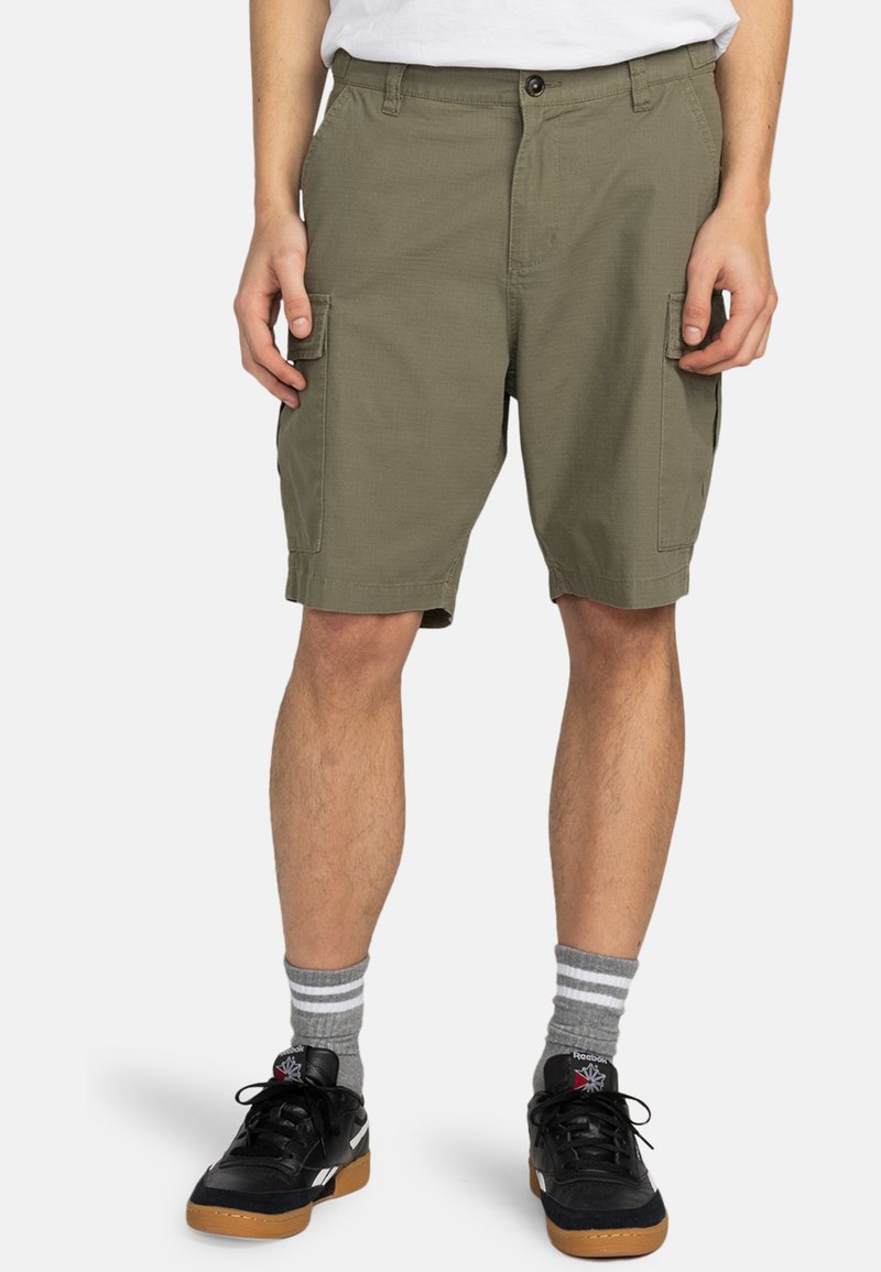 Pantalones cortos cargo color caqui con múltiples bolsillos, corte recto y cierre de botón. Combinados con zapatillas negras y calcetines gris rayados.