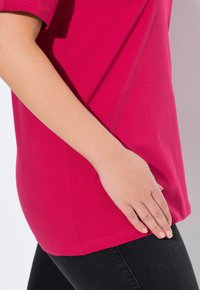 T-shirt fuchsia à manches courtes avec une coupe droite et un tissu en coton doux et lisse. Associé à un denim noir, mettant en valeur les contours.