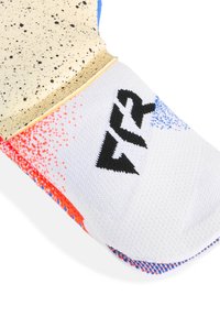 Gros plan sur un gant de boxe coloré avec une sangle de poignet beige tachetée et un tissu blanc affichant le logo "Fly" en noir avec des accents rouge et bleu.