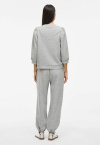 Grauer Sweatshirt mit Dreiviertelärmeln und gerippten Bündchen, kombiniert mit passenden grauen Jogginghosen, elastischen Bündchen und weißen Sneakern.