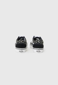 Baskets en nubuck noir avec des accents blancs, présentant un motif de pois noirs sur le talon et un col rembourré pour le confort.