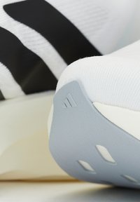 Gros plan d'une semelle blanche de sneaker avec un talon gris texturé arborant le logo Adidas et des bandes noires sur la tige de la chaussure.
