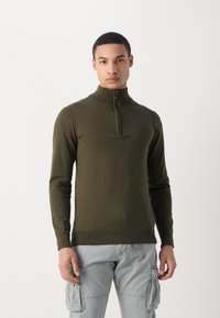 Pull-over vert olive avec fermeture éclair, col montant, design ajusté, poignets et ourlet côtelés, fabriqué en tissu tricoté doux et texturé.