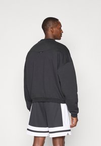 Sort sweatshirts med høj hals og sænkede skuldre, med ribbet kant og et lille mærke på ryggen. Sammen med grå shorts.