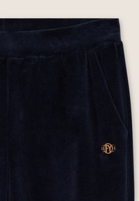 Pantaloni tuta in corduroy blu navy con un tessuto testurizzato, vita elastica, tasche laterali e un accento dorato con il logo a sinistra.