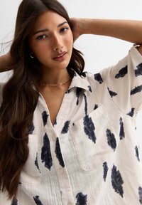 Lange mouwen, gekraagde blouse in crème met marineblauwe penseelstreken. Bevat twee borstzakken en heeft een ontspannen pasvorm. Lichtgewicht stoftextuur.