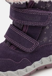 Botte d'hiver violette avec tige en suède, deux sangles velcro, bordure en polaire et semelle en caoutchouc texturé. Comprend des accents métalliques sur le fût.