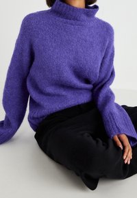 Paarse, zachte trui met een hoge kraag en lange mouwen, met een losse pasvorm en een zachte textuur, gecombineerd met een zwarte broek.