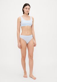 Costum de baie de culoare bleu deschis, realizat dintr-un material moale și elastic. Top scurt cu un bandaj lat; partea de jos a costumului de baie cu talie joasă prezintă un accent cu logo pe lateral.