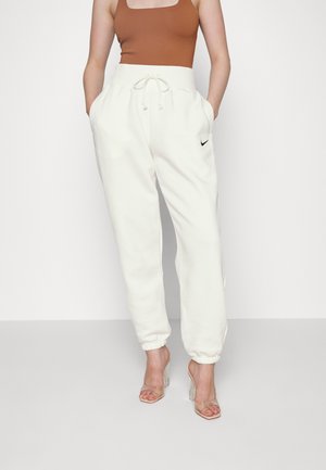 Balti sporta bikses ar elastīgām šķipsnām un auklu jostu, ar mazu melnu Nike logo. Kombinētas ar brūnu topu un caurspīdīgām papēžkurpēm.